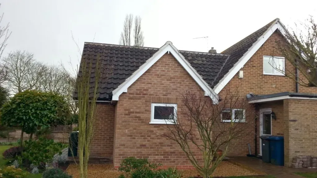 A residential house featuring a dark tiled pitched roof with white fascias and gutters, showcasing a typical property serviced by Bridgeford Roofing.