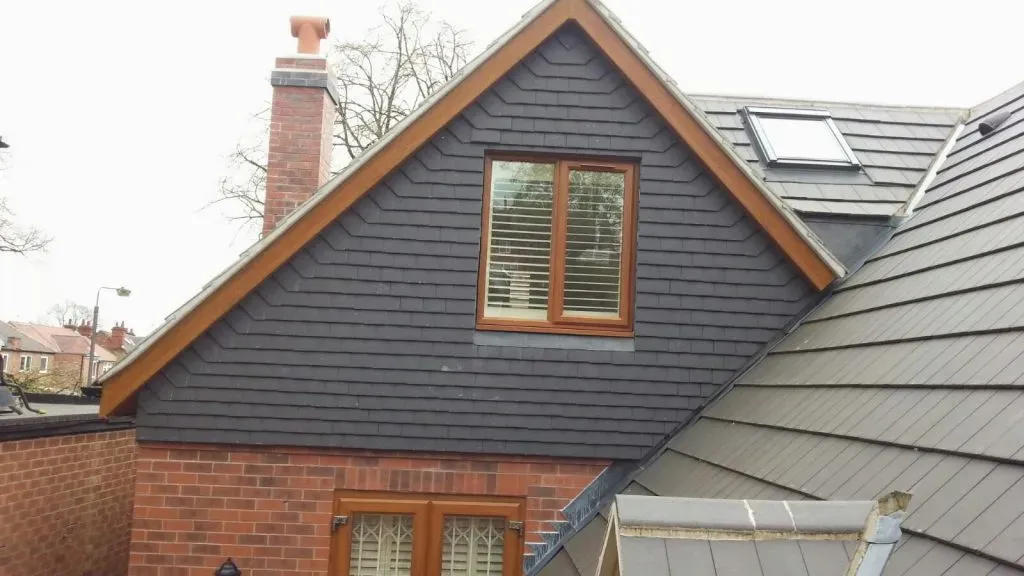 Side view of a house roof with dark grey tiles, a dormer window, and a Velux skylight.