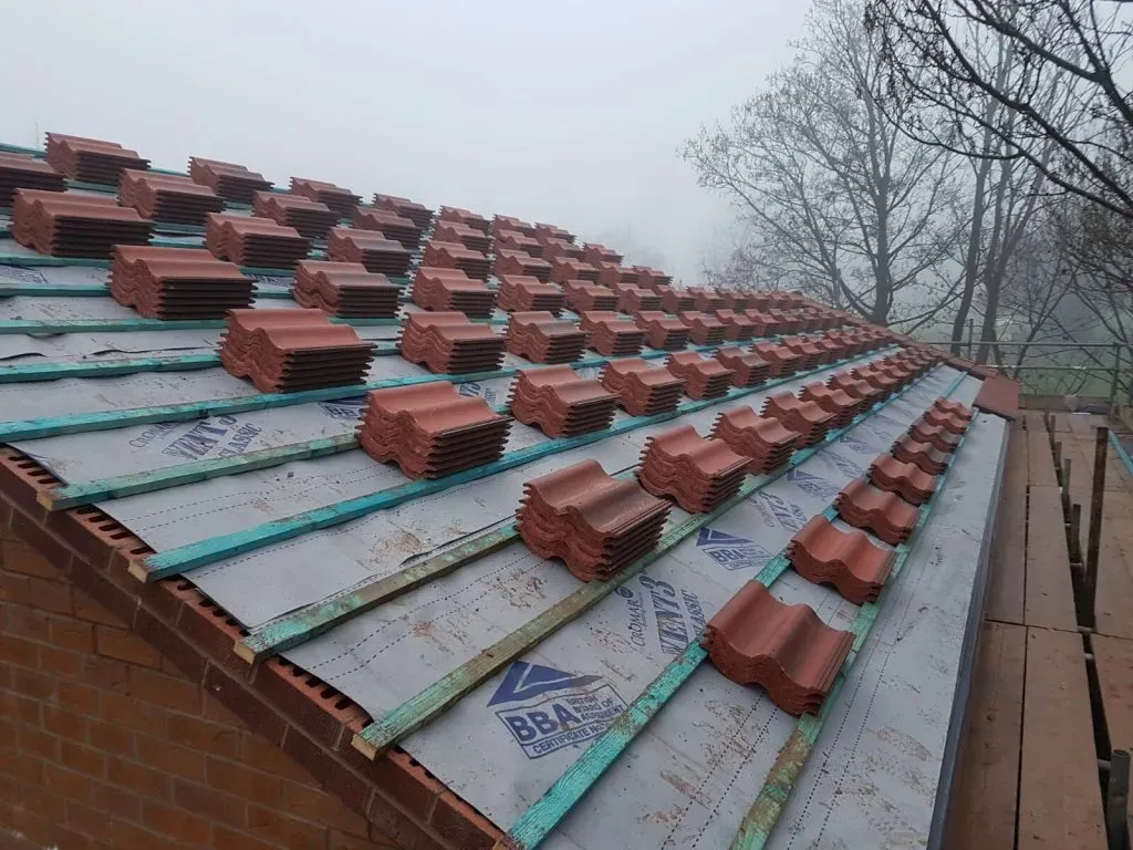 New pitched roof installation in progress with stacks of red tiles, breathable membrane, and timber battens.