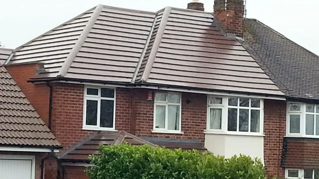A residential house with a new brown tiled pitched roof on the left, contrasting with an older, mossier roof on the right.