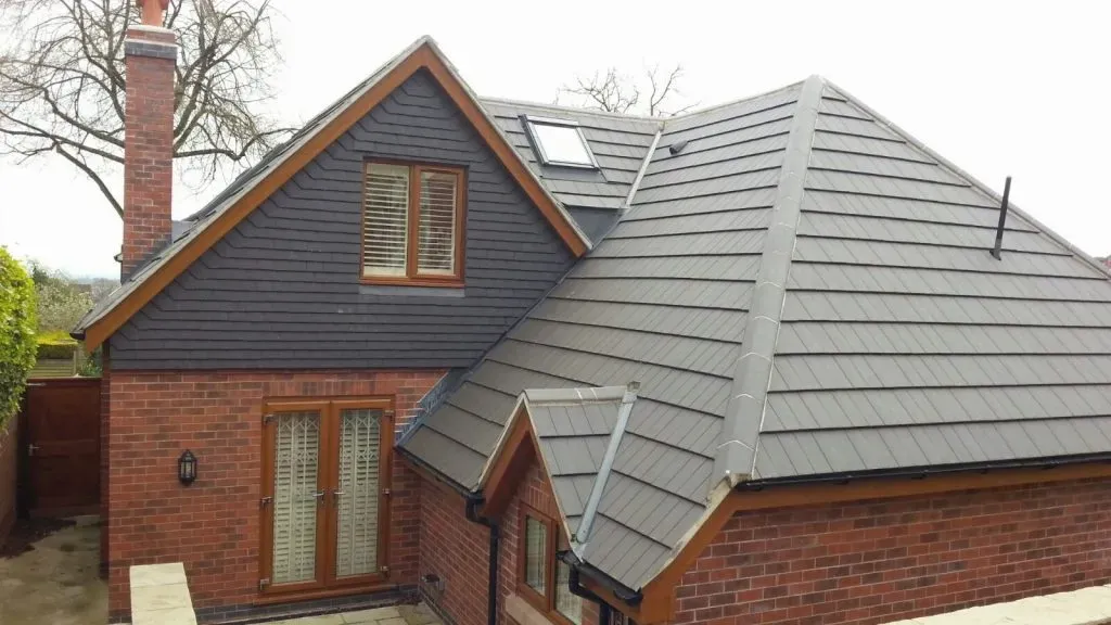 A house with a newly installed dark grey pitched roof, a Velux skylight, a red brick chimney, and contrasting dark grey slate-effect cladding on the dormer.