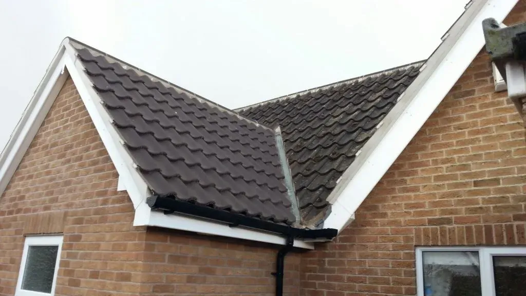Pitched roof with dark tiles, showing a cleaner section contrasting with a mossy section, with a lead valley and roofline components visible.