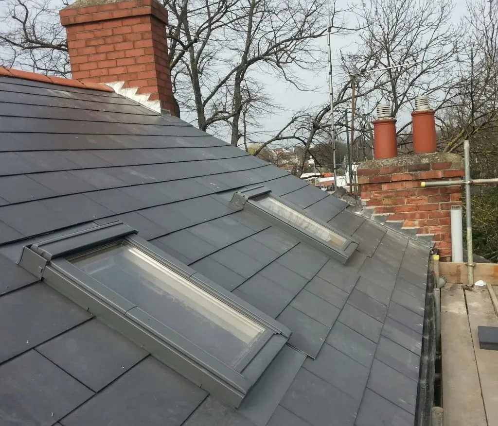 Newly installed Velux windows on a dark grey tiled pitched roof, next to a brick chimney.